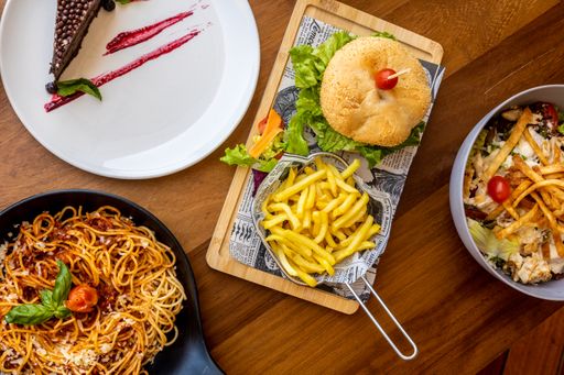 A top view of a table in a cafe full of food including plates of pasta, salads, and a slice of cake