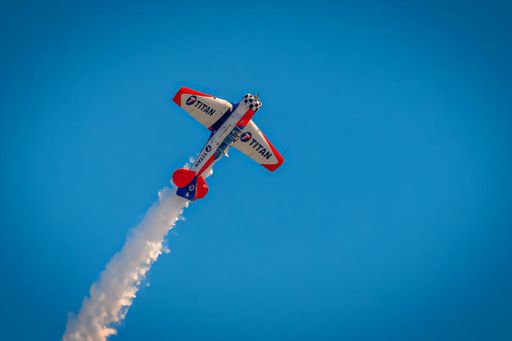 Aerobatic plane performing a vertical climb with smoke trail against a clear blue sky.