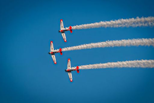 Aerobatic team performing synchronized flight in clear blue sky with smoke trails.