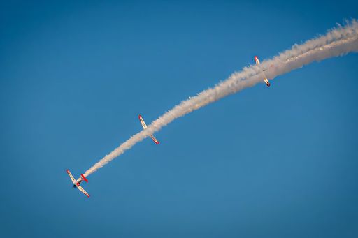 Aerobatic planes perform in clear blue sky, leaving smoke trails in a synchronized airshow display.