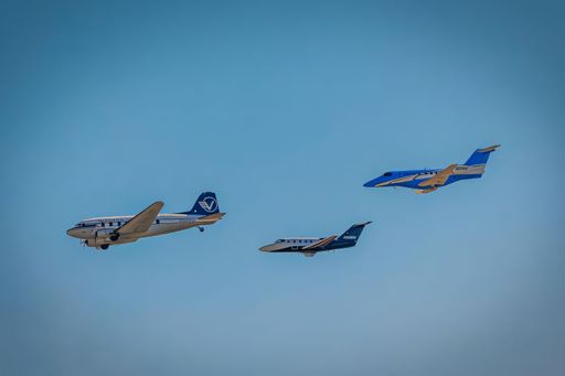 Three vintage airplanes in formation flight against a clear blue sky, showcasing aviation history and teamwork.