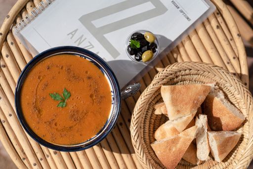 A top view closeup of a soup in a bowl and bread pieces next to it on a wooden table in morocco
