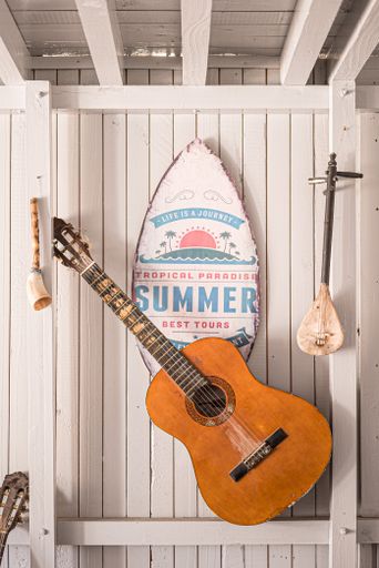 A cozy view of an acoustic guitar hanging on the wall in front of the surfing board decoration
