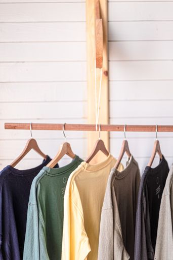 A view of a couple of colorful t-shirts with hangers hanging on the wooden pole in the room