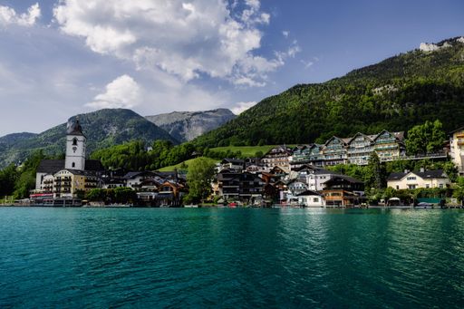 Scenic view of St. Wolfgang village by Lake Wolfgang with mountains and a church under a partly cloudy sky in Austria.