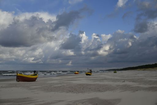 Yellow boats on a sandy beach under a dramatic cloudy sky, with waves crashing in the background, creating a serene coastal scene.