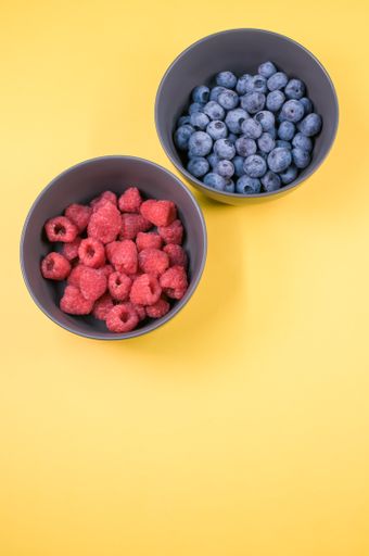 The bowls of raspberries and blueberries isolated on a yellow background with free space for text