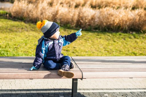Small two years old boy sitting on a wooden bench and pointing at something in the Rataje park.