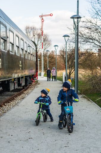 Young boys on bicycles riding next o a old exposition train wagon in the Rataje park.