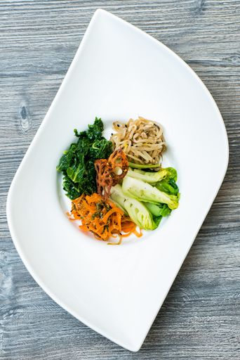 A vertical shot of sliced vegetables and noodle on a white modern plate