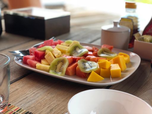 A vibrant plate of sliced tropical fruits including kiwi, mango, pineapple, and watermelon on a wooden table.