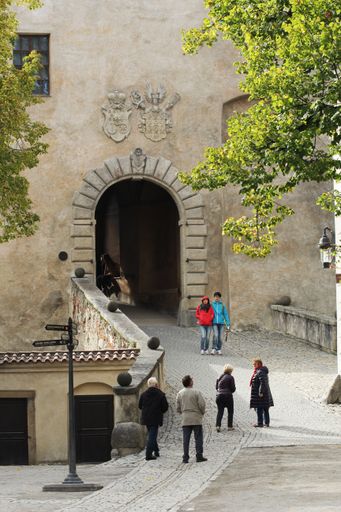 The arched entrance of State Castle of Cesky Krumlov with two coats of arms above and people walking