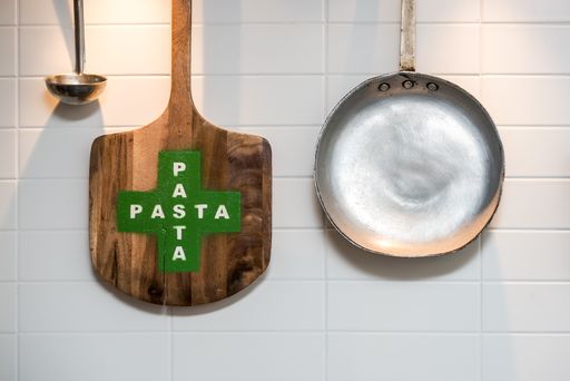 A pan, wooden peel and a metal soup spoon hanging on a white wall