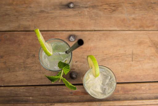 An overhead shot of drinks with lemon, vegetable leaf and black straw on a wooden surface