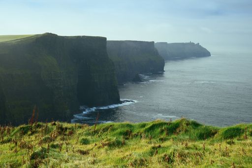 Majestic view of the Cliffs of Moher in Ireland with lush green grass and a misty sea view.