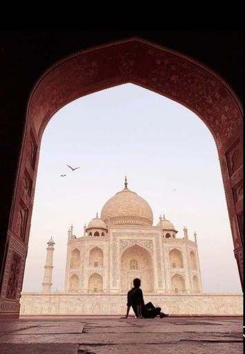 A man sitting in front of the white marble mausoleum of the Taj Mahal in Agra, India