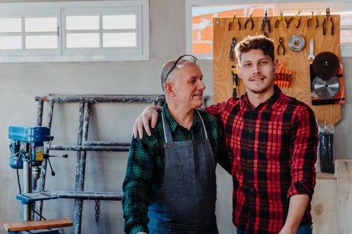 A senior carpenter hugging his young student