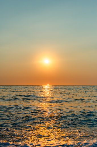 A gorgeous sunset in Lefkada, Greece - vertical shot of the golden sun shining over the calm sea in a gradient sky
