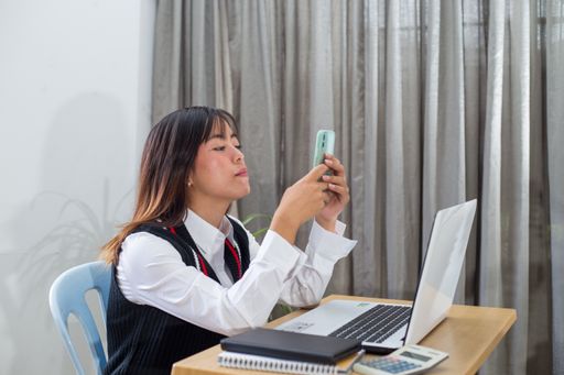 A closeup shot of a Southeast Asian young woman looking at her phone in front of her computer