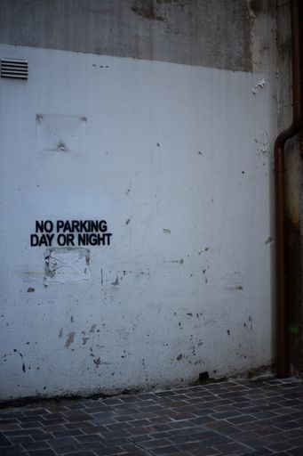 A vertical shot of a building exterior wall with "No Parking Day or Night" text