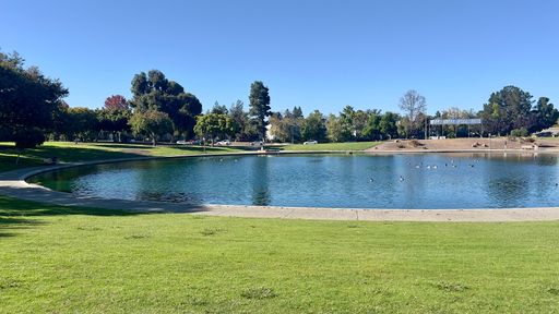 A scenic park with a tranquil lake, lush trees, and a bright blue sky.