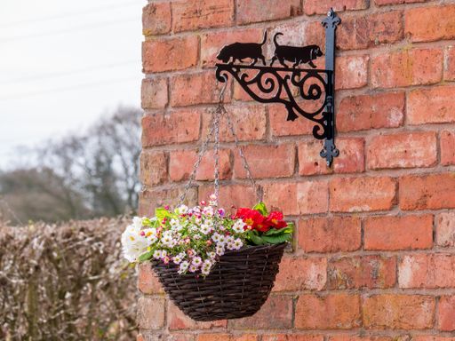 A closeup shot of a basket of red and pink flowers hanging from a brick wall
