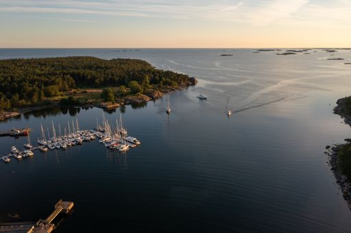 Aerial drone view of a boat arriving to a guest harbor at the Jussaro island, summer evening, in Tammisaari archipelago, Uusimaa, Finland