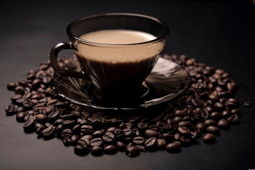 A glass cup of coffee surrounded by roasted coffee beans on a dark background, highlighting the rich aroma and texture.