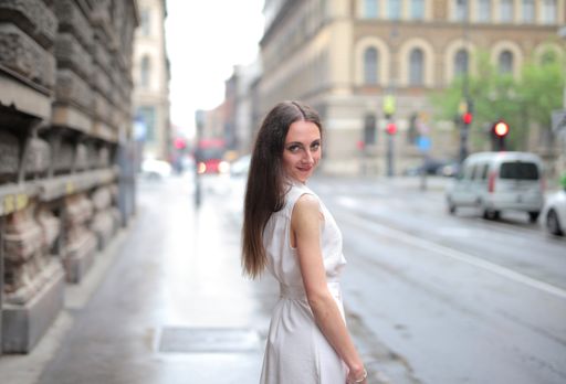 A selective focus shot of a beautiful female in a white dress looking over her shoulder in a street