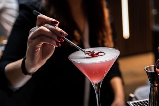 A special pink cocktail with flower petal on top served by a barista