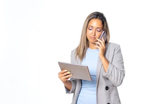 A business woman talking on the phone looking at the tablet she holds with the white background
