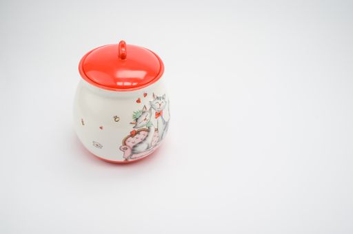 A small white and red ceramic container with a lid for coffee, sugar or tea isolated on white