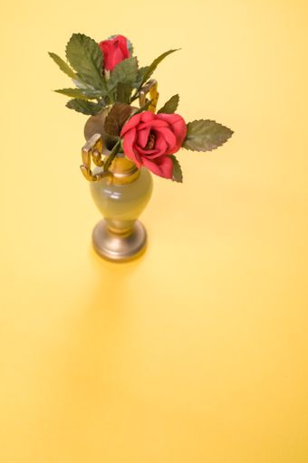 A top view of red decorative roses in a small vintage vase on a yellow background with a copy space