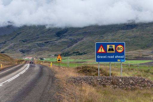 A highway through the mountains with a warning sign saying 'gravel road ahead'