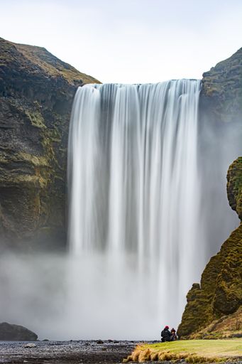 A mesmerizing view of a waterfall between green hills in Skogafoss, Iceland