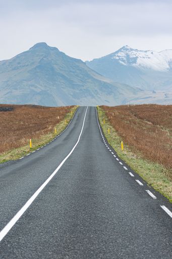 A scenic view of a straight country road between agricultural field and mountain landscape in Iceland