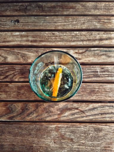 A vertical shot of the glass filled with water and a piece of orange in it on a wooden surface.