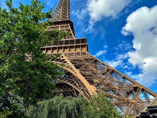 A low angle shot of the Eiffel Tower with lush green trees and a vibrant blue sky in Paris, France