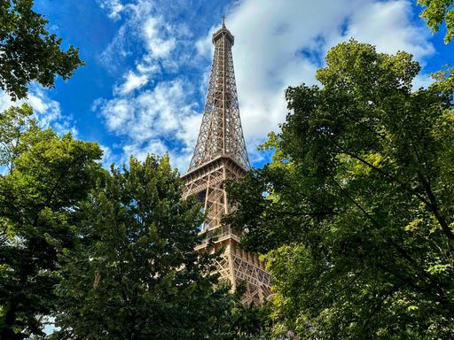 A low angle shot of the Eiffel Tower with lush green trees and a vibrant blue sky in Paris, France