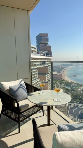 Luxury balcony view with modern architecture and beach scenery in Dubai, featuring comfortable seating and drinks.