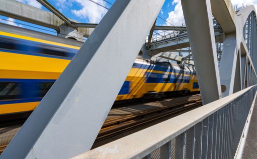 A closeup shot of the steel structure of a railway bridge with steel beams and a crossing train