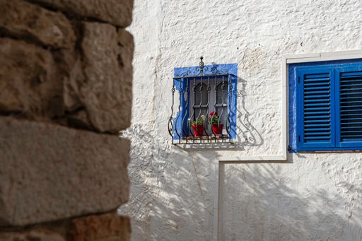 A closeup shot of small blue windows on a white house with a Greek-style