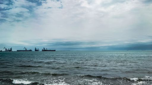 Calm sea with distant cargo ships under a cloudy sky, capturing a serene maritime scene.