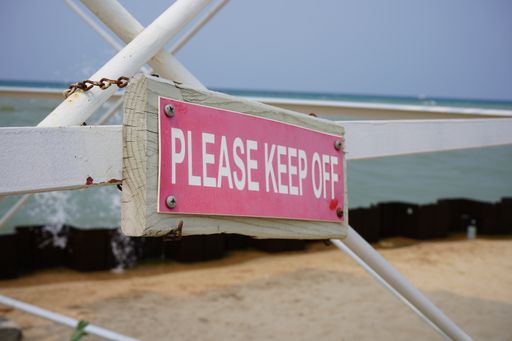 A closeup of a wooden beach sign that reads "please keep off" on a bright summer day