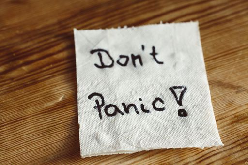 A high angle shot of a Don't panic note on a piece of paper on a wooden surface - panic because of Covid-19