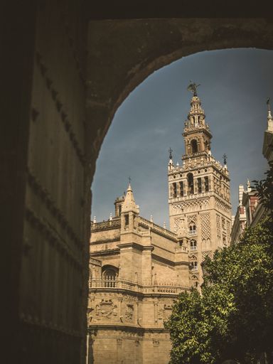 A scenic view of the Giralda tower framed by an archway in Seville, Spain, under a clear sky