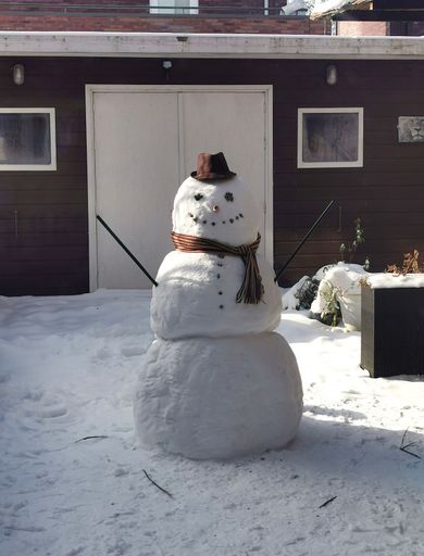 A snowman in a snowy area in front of a wooden building