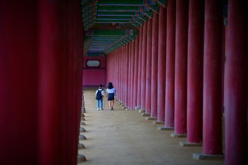 Two people walking through the exterior hallway of the Gyeongbokgung Palace, South Korea