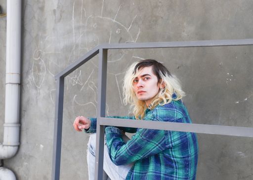 An attractive Armenian guy sitting on the stairs next to a grey wall while looking at the camera