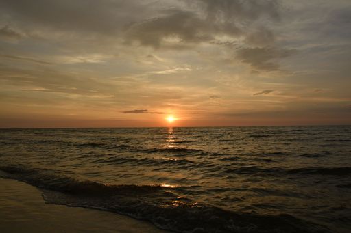 Serene sunset over calm ocean waves with a golden sky reflecting on the water surface, creating a tranquil seascape.